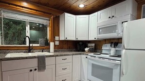 A modern kitchen with white cabinets, a granite countertop, a stainless steel sink, a microwave, a stove, and a refrigerator.