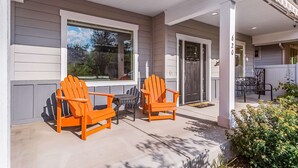 Eine überdachte Veranda mit zwei Adirondack-Stühlen, einem Fenster und einer Tür.