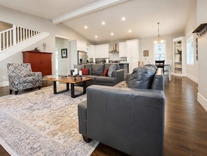 A spacious living room with a grey sofa, patterned armchair, and a coffee table. A staircase leads to an upper level. - Spacious CDA Getaway | Fire Pit, BBQ & Backyard (Coeur d'Alene)