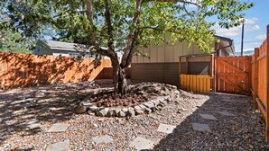 Un patio trasero con un árbol, cerca de madera y un camino de grava.