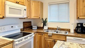Una cocina moderna con armarios de madera, microondas integrado, estufa, lavaplatos y cafetera.