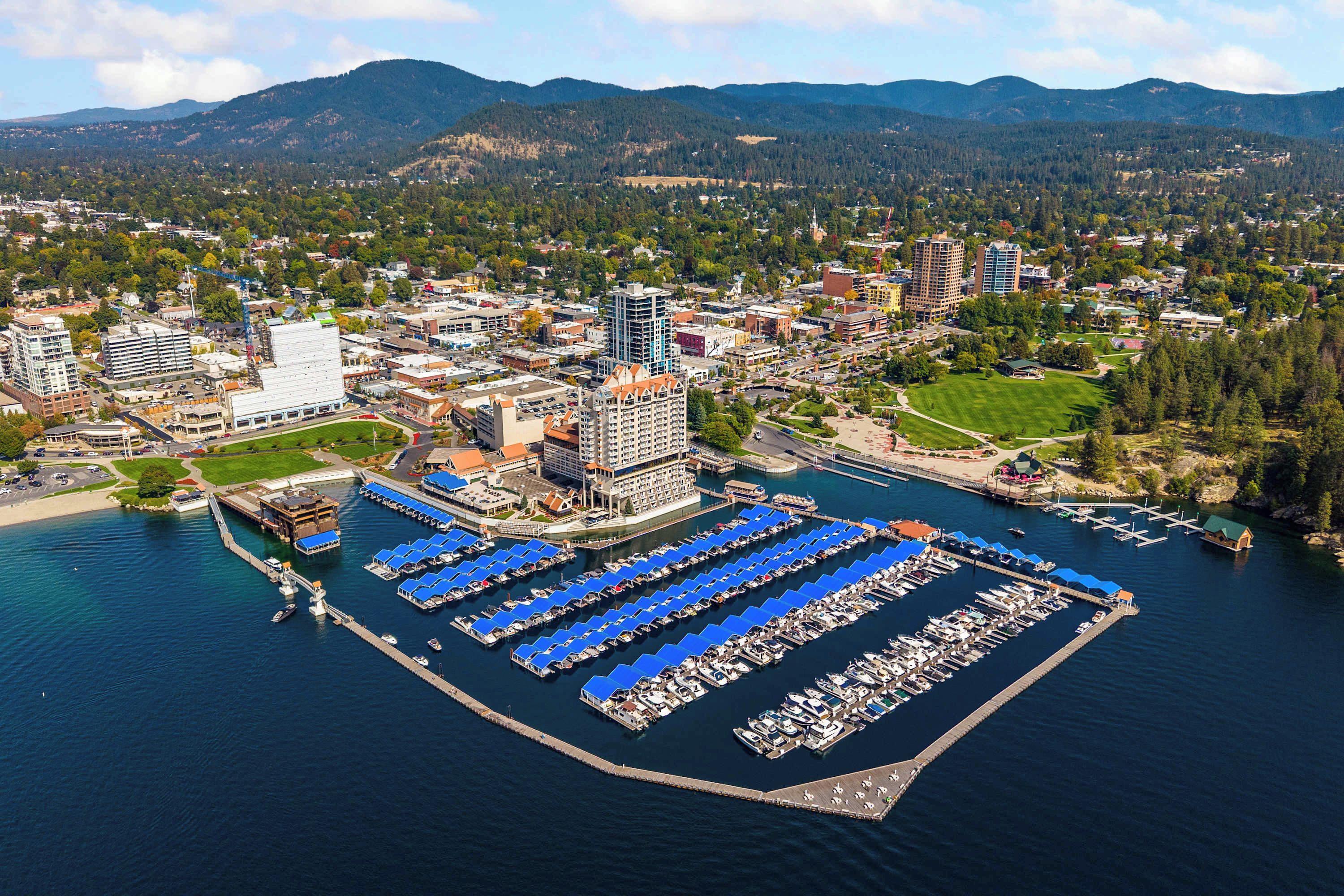 A marina with numerous docked boats, a central building with a blue roof, and surrounding residential and commercial buildings.