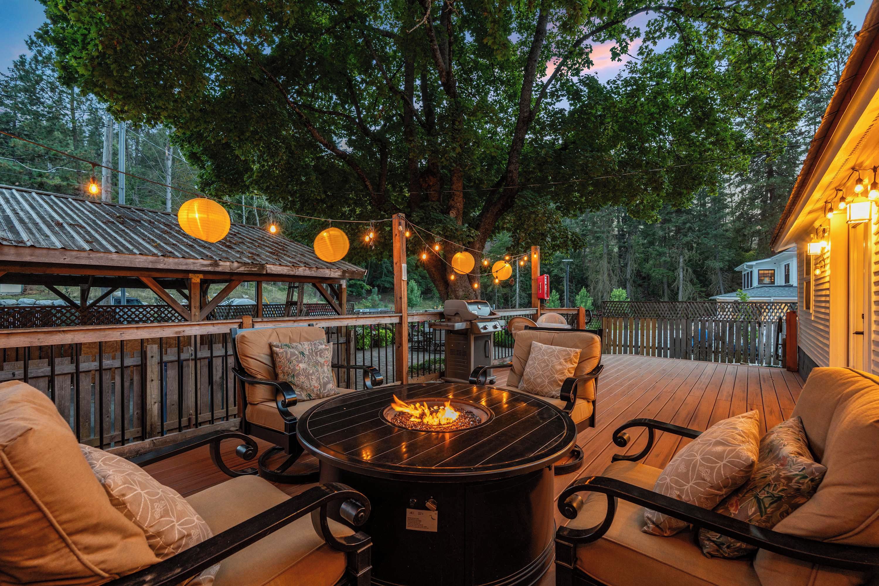 An outdoor patio with a round table and chairs, a fire pit, string lights, and a view of a house.