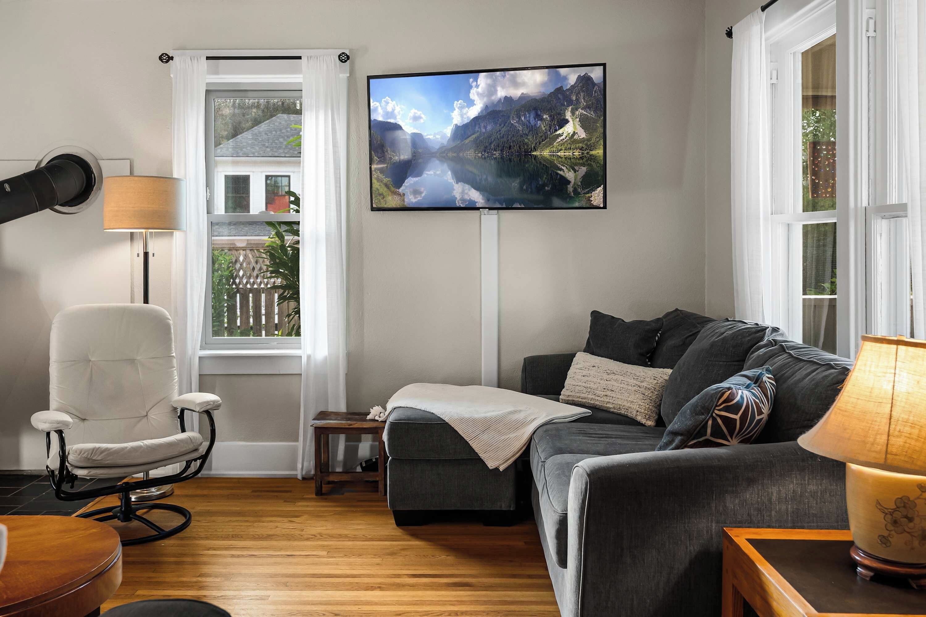 A living room with a sofa, chair, and a TV mounted on the wall displaying a mountain landscape.