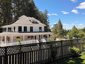 A two-story white house with a covered porch, a fenced yard, and a mountainous backdrop.