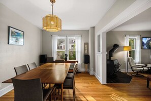 Un comedor amplio con una larga mesa de madera y sillas, una lámpara colgante y vistas al exterior a través de grandes ventanas.
