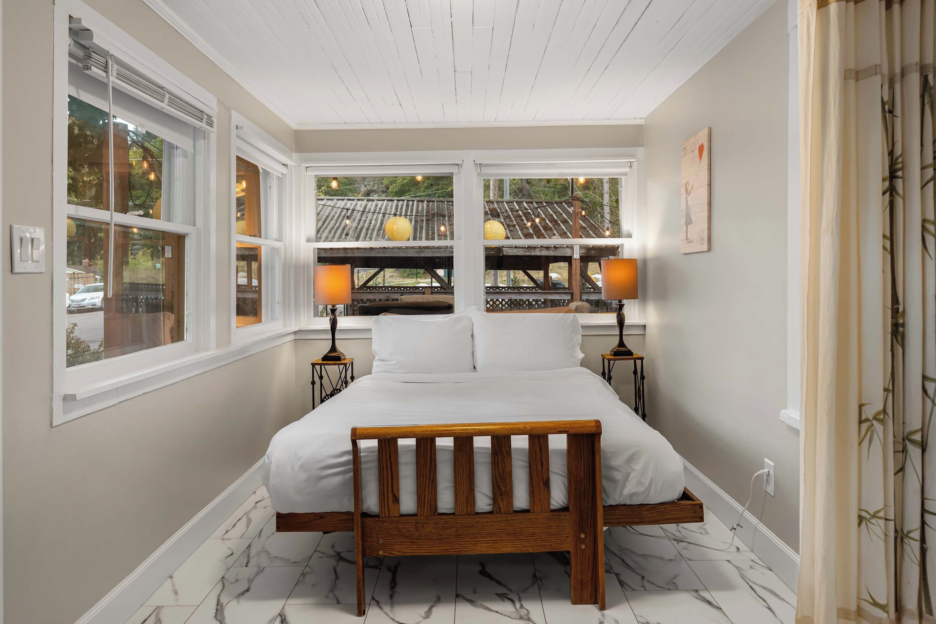 A bedroom with a bed, two bedside tables, a window with a view, and a ceiling with wooden beams.