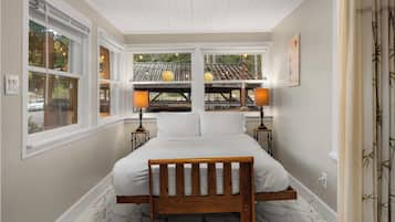 A bedroom with a bed, two bedside tables, a window with a view, and a ceiling with wooden beams.