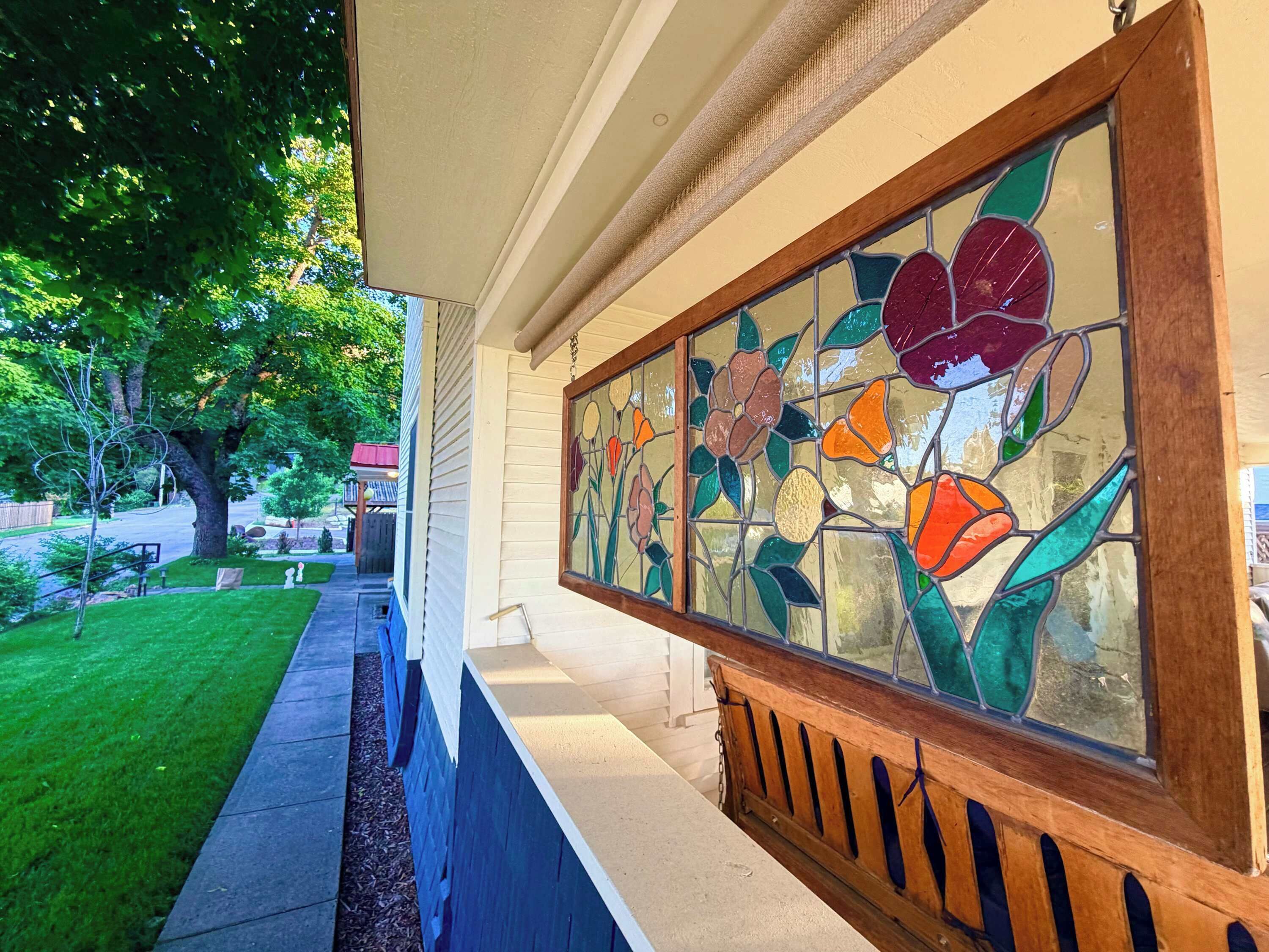 Porch detail: vivid stained-glass floral panel on the hanging swing, overlooking the tree-lined front yard