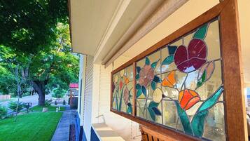 Porch detail: vivid stained-glass floral panel on the hanging swing, overlooking the tree-lined front yard