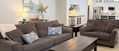 A living room with two sofas, a coffee table, and a dining area with a chandelier.