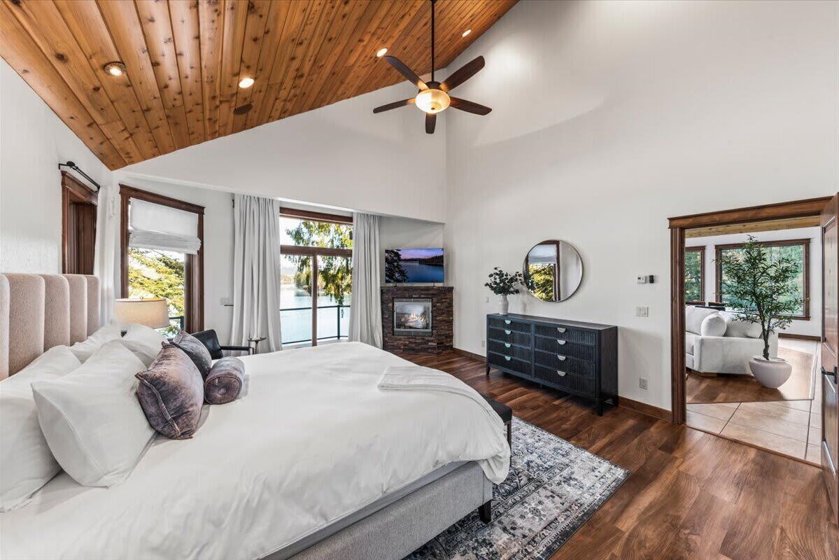 A spacious bedroom with a large bed, a fireplace, a ceiling fan, and a view of the outdoors.