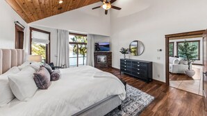 A spacious bedroom with a large bed, a fireplace, a ceiling fan, and a view of the outdoors. - Lakefront Luxury | Dock, Hot Tub & Entertainment (Hayden Lake)