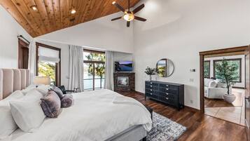 A spacious bedroom with a large bed, a fireplace, a ceiling fan, and a view of the outdoors.