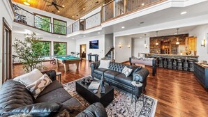 A spacious living area with a pool table, leather sofas, and a kitchen with a bar. - Lakefront Luxury | Dock, Hot Tub & Entertainment (Hayden Lake)