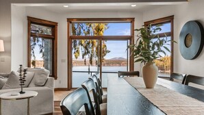A dining area with a large table, chairs, and a view of a lake and mountains. - Lakefront Luxury | Dock, Hot Tub & Entertainment (Hayden Lake)