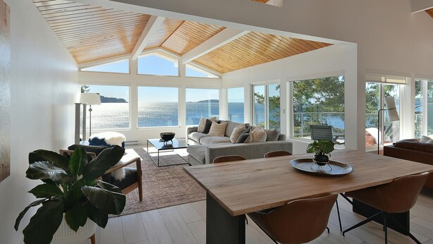 A spacious living area with a large wooden ceiling, a wooden dining table, and a view of the sea. - Waterfront Serenity on the Sunshine Coast BC*
*90 day min rent due to BC Law (Halfmoon Bay)