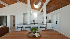 A modern kitchen with white cabinets, a central island, and a dining area with a wooden table and chairs. - Waterfront Serenity on the Sunshine Coast BC*
*90 day min rent due to BC Law (Halfmoon Bay)