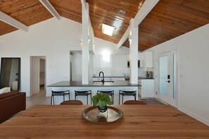 Una cocina moderna con armarios blancos, una isla central y un comedor con mesa y sillas de madera.
