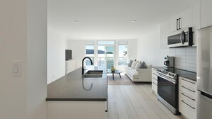 A modern kitchen with a large island, a dining area with a sofa, and a view of the sea. - Waterfront Serenity on the Sunshine Coast BC*
*90 day min rent due to BC Law (Halfmoon Bay)