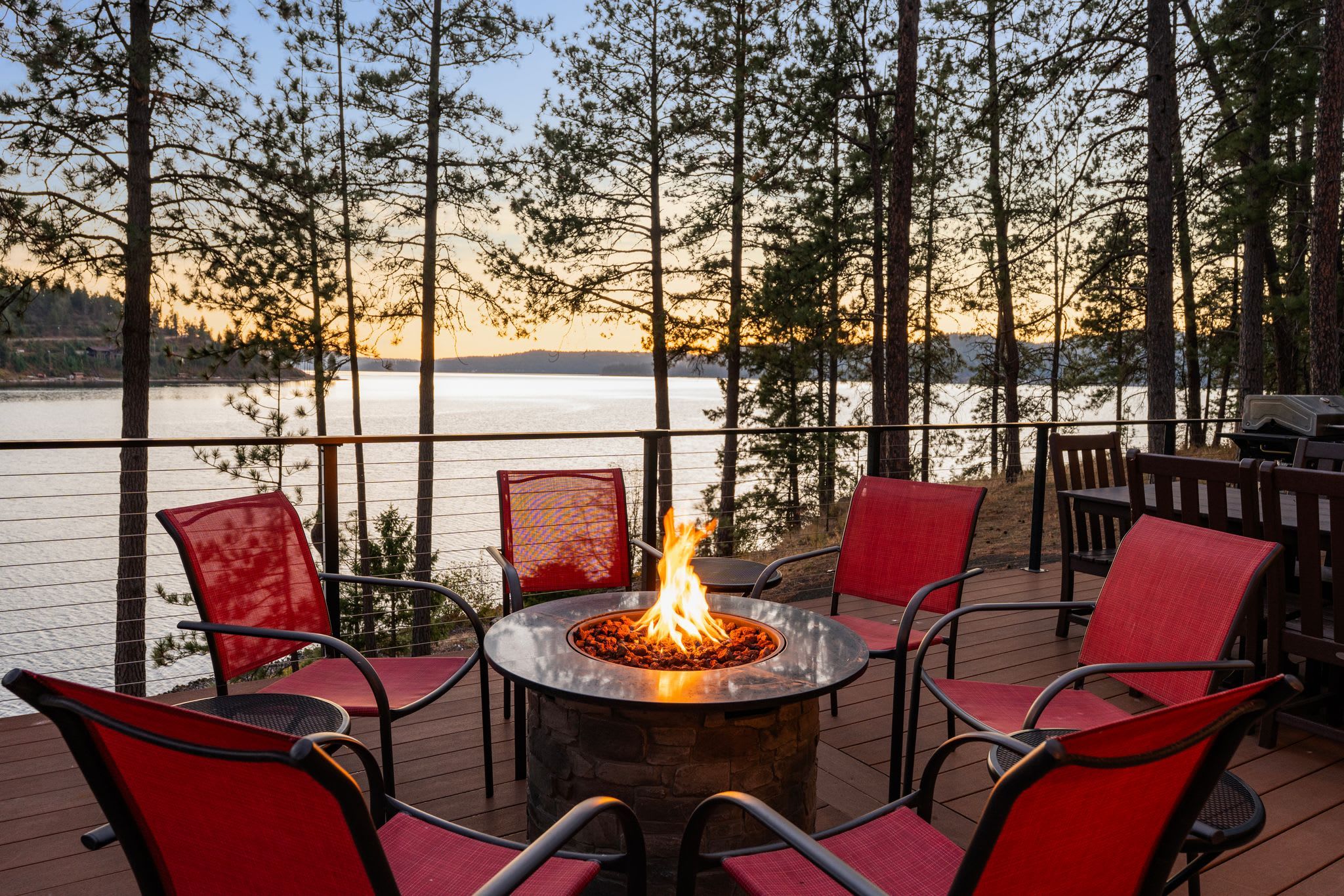 Fire pit on the deck with the lake beyond the pines