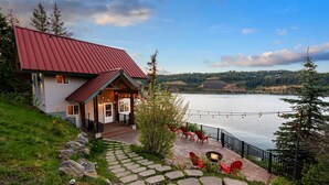 A house with a red roof, a deck with outdoor furniture, and a view of a lake.