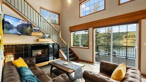 A spacious living area with a fireplace, a large flat-screen TV, and a balcony with a scenic view.