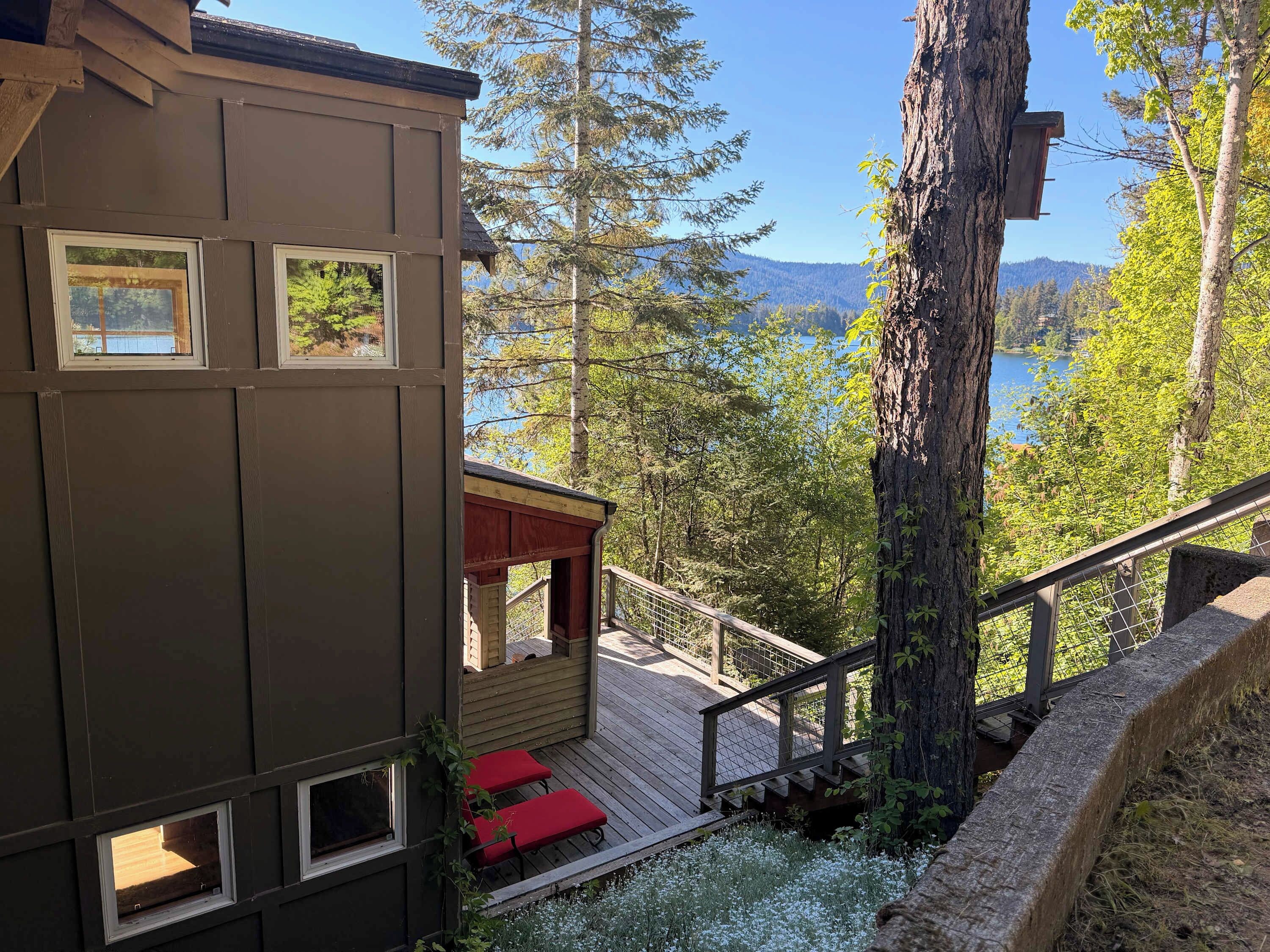 A cabin with a deck, a small red-roofed structure, and a view of a lake and forest.
