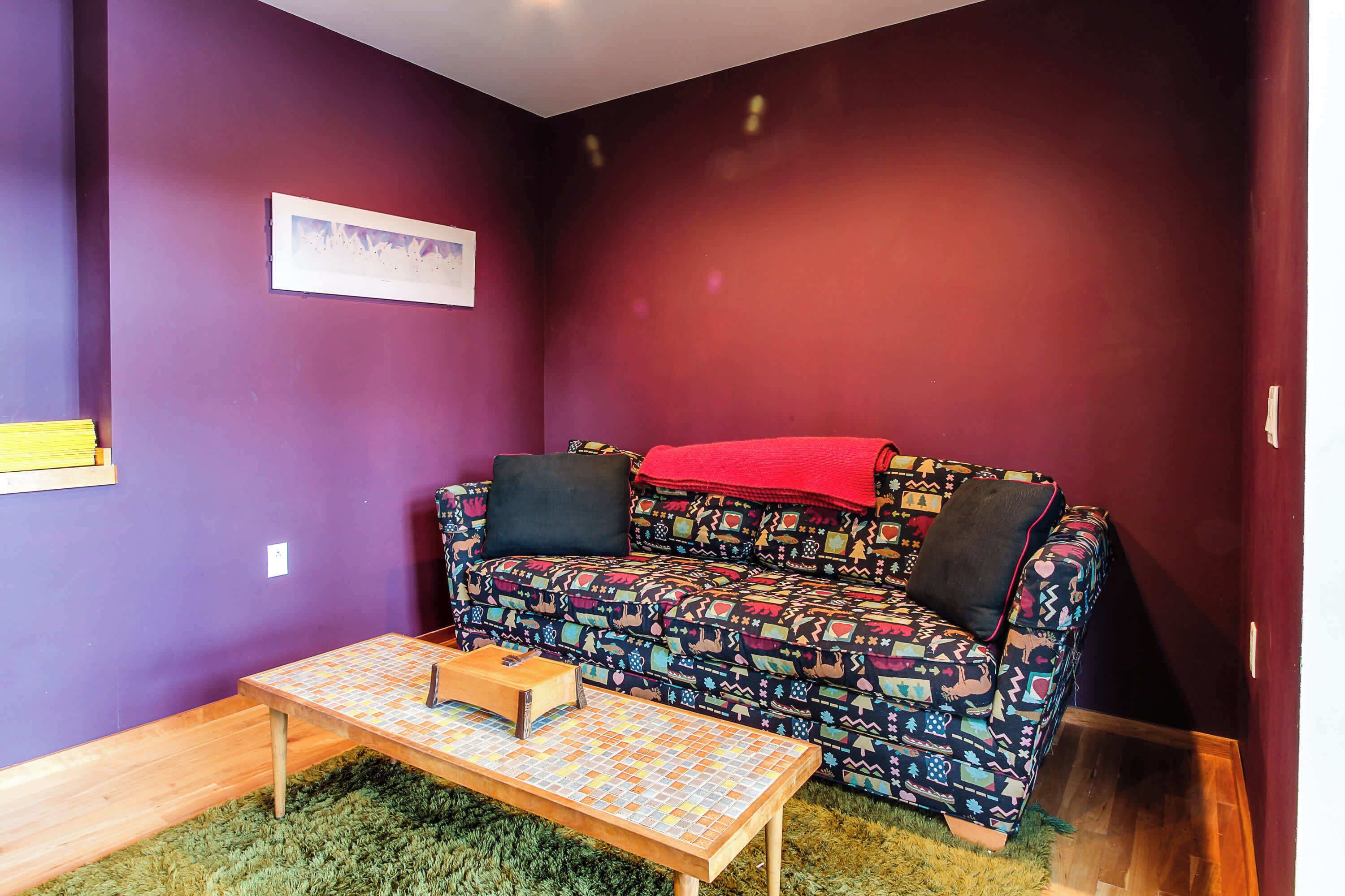 A room with a patterned sofa, a small wooden table, and a green rug.