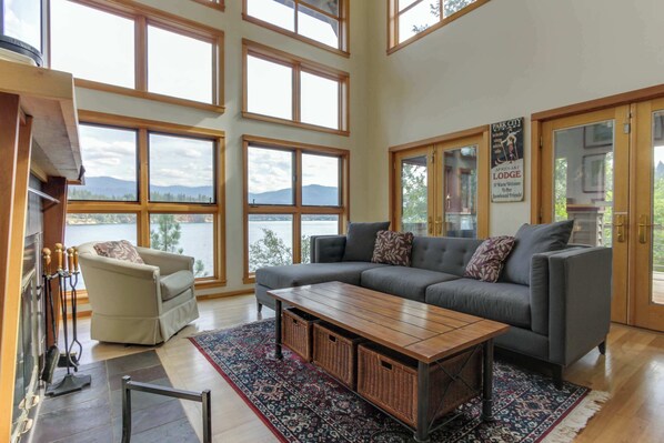 A spacious living room with a large gray sofa, a wooden coffee table, and a view of mountains through large windows.