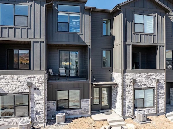 A multi-story residential building with a stone facade, large windows, and a balcony.