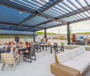 An outdoor patio area with tables and chairs, a covered seating area, and a view of the surrounding landscape.