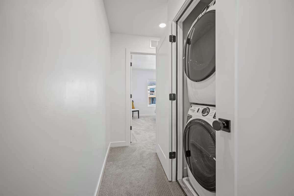 A laundry room with two front-loading washers and dryers, a carpeted floor, and a white interior.