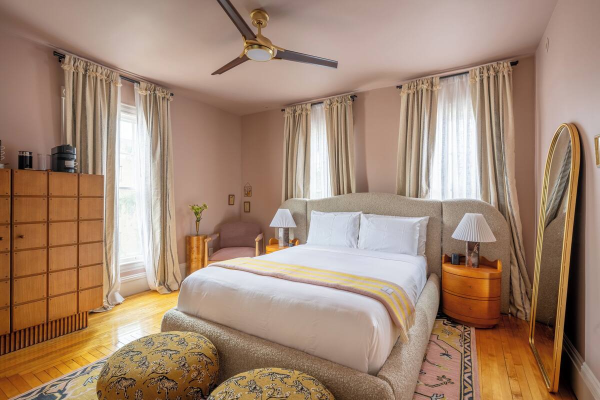 A bedroom with a bed, bedside lamps, a mirror, a wardrobe, and a ceiling fan.