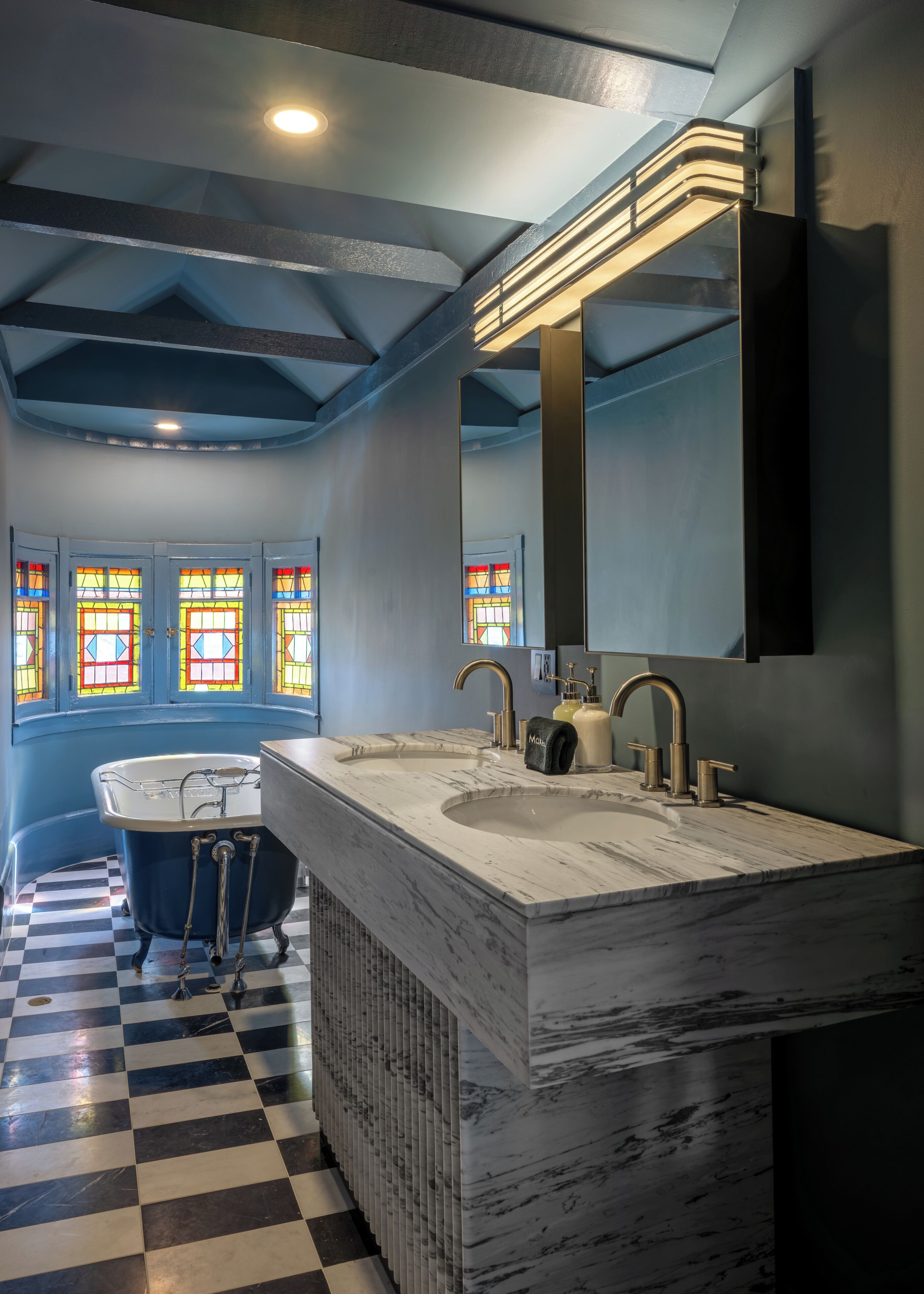 A bathroom with a checkered floor, a bathtub, a double sink with a marble countertop, and a large mirror.