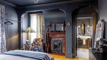 Une chambre à coucher comprenant un lit, une chaise, une cheminée, un miroir et une salle de bain visible à travers une arche.