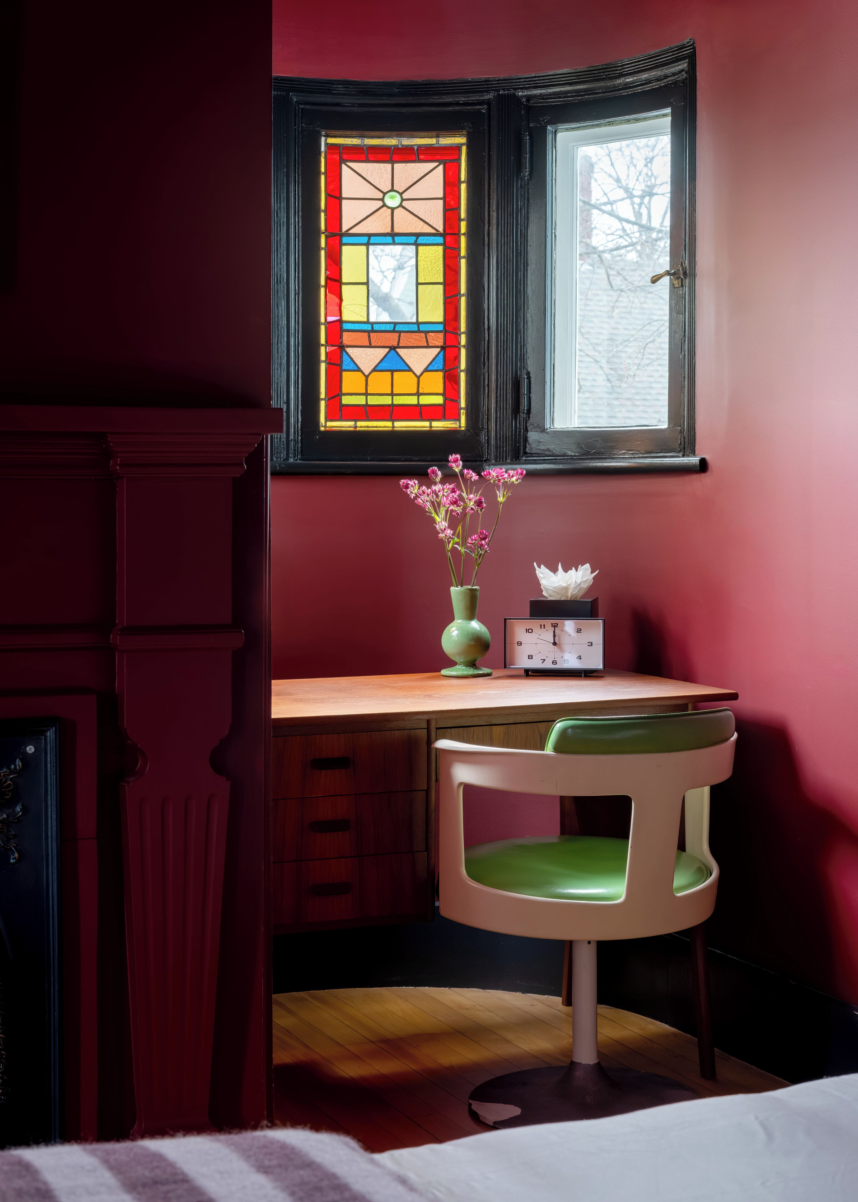 A room with a desk, chair, and a stained glass window.