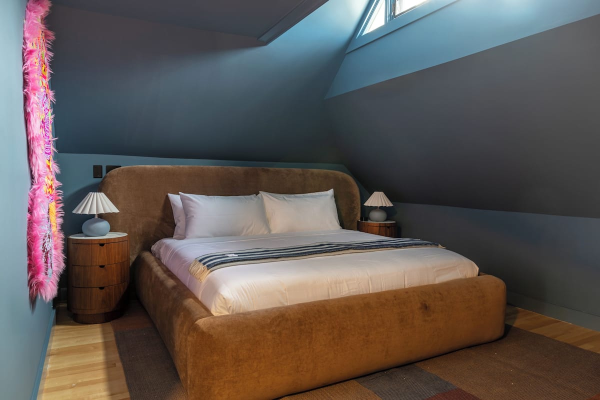 A bedroom with a brown bed, two bedside tables with lamps, a pink decorative item, and a skylight.