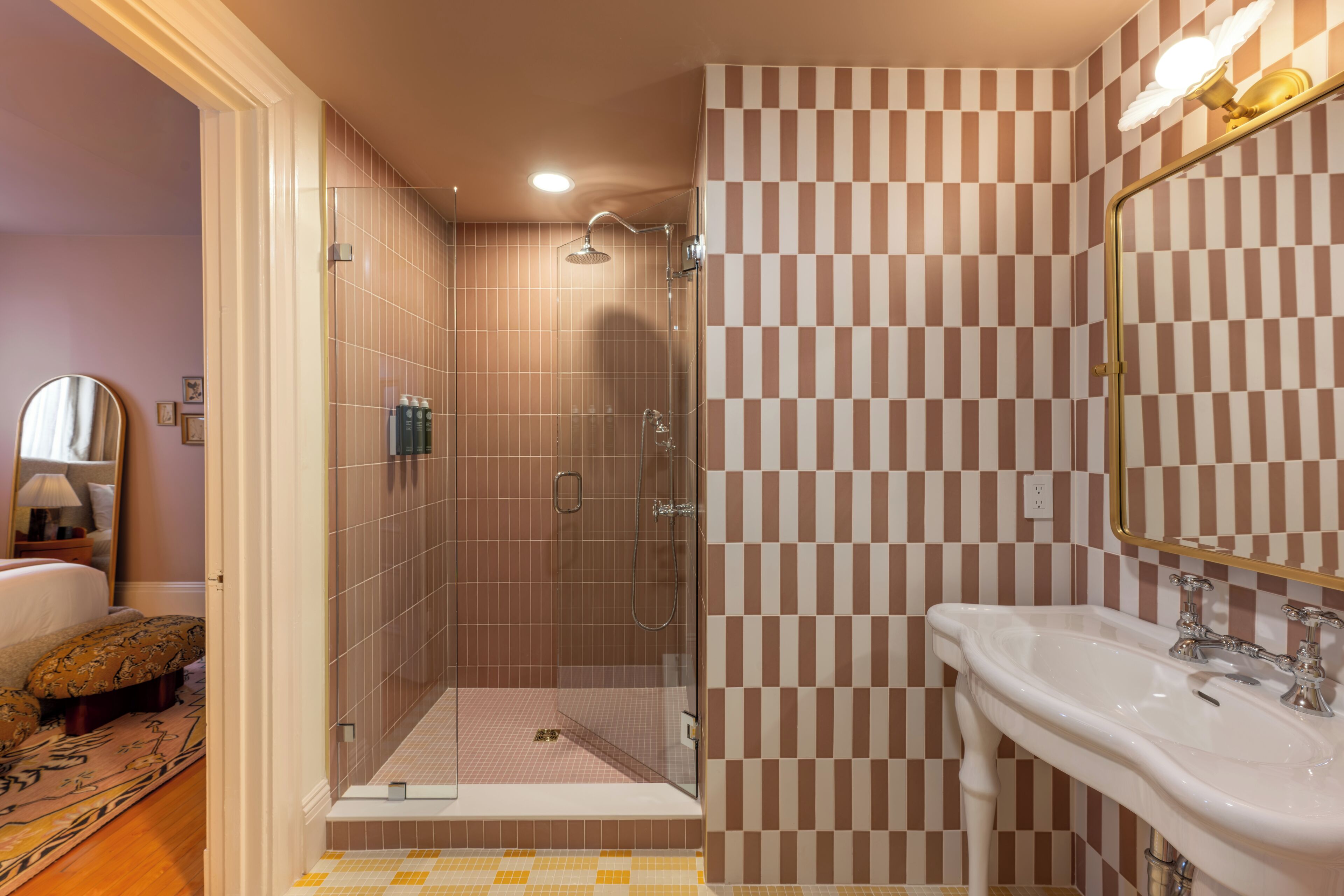 Ein Badezimmer mit einer Wand aus Schachbrettfliesen, einer Duschkabine aus Glas und einem weißen Waschbecken mit goldfarbenem Wasserhahn.