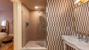 Ein Badezimmer mit einer Wand aus Schachbrettfliesen, einer Duschkabine aus Glas und einem weißen Waschbecken mit goldfarbenem Wasserhahn.