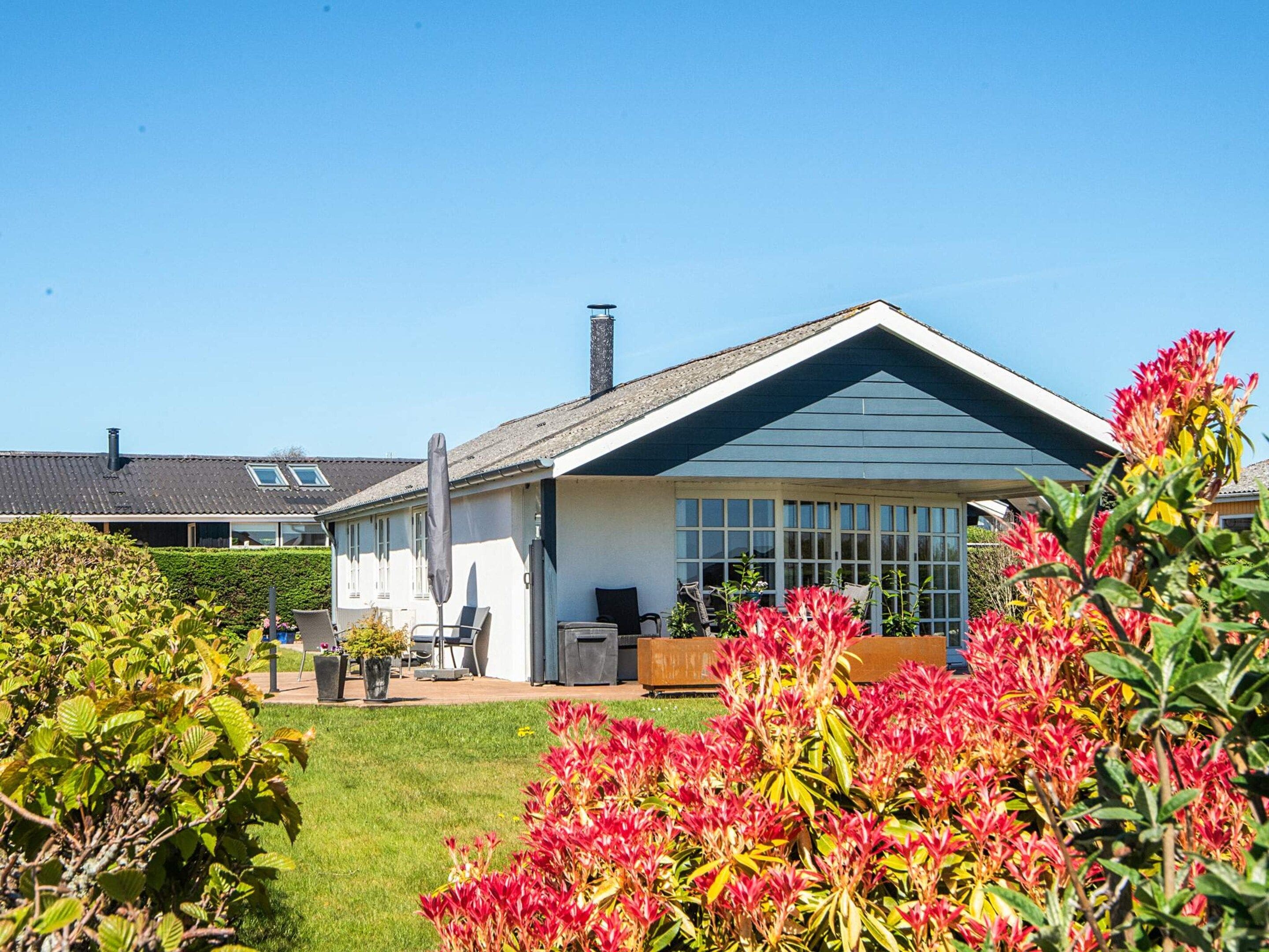 A house with a large window, a chimney, and a garden with red flowers.