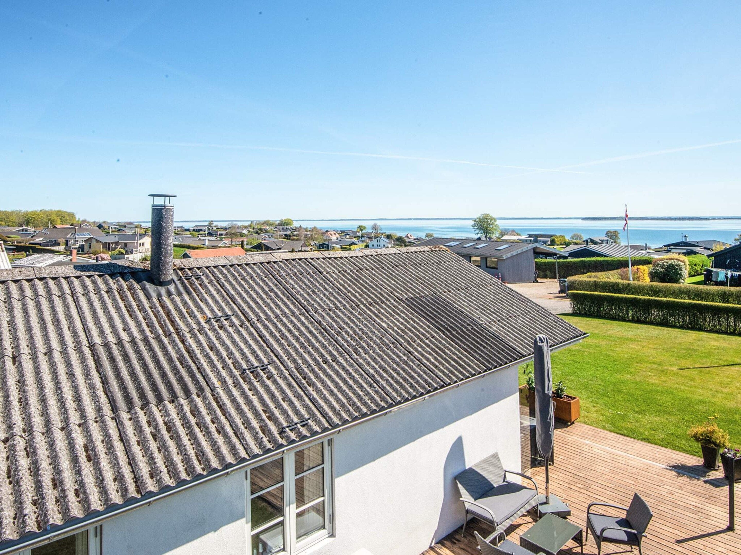 A residential building with a tiled roof, a balcony with outdoor furniture, and a view of a body of water.