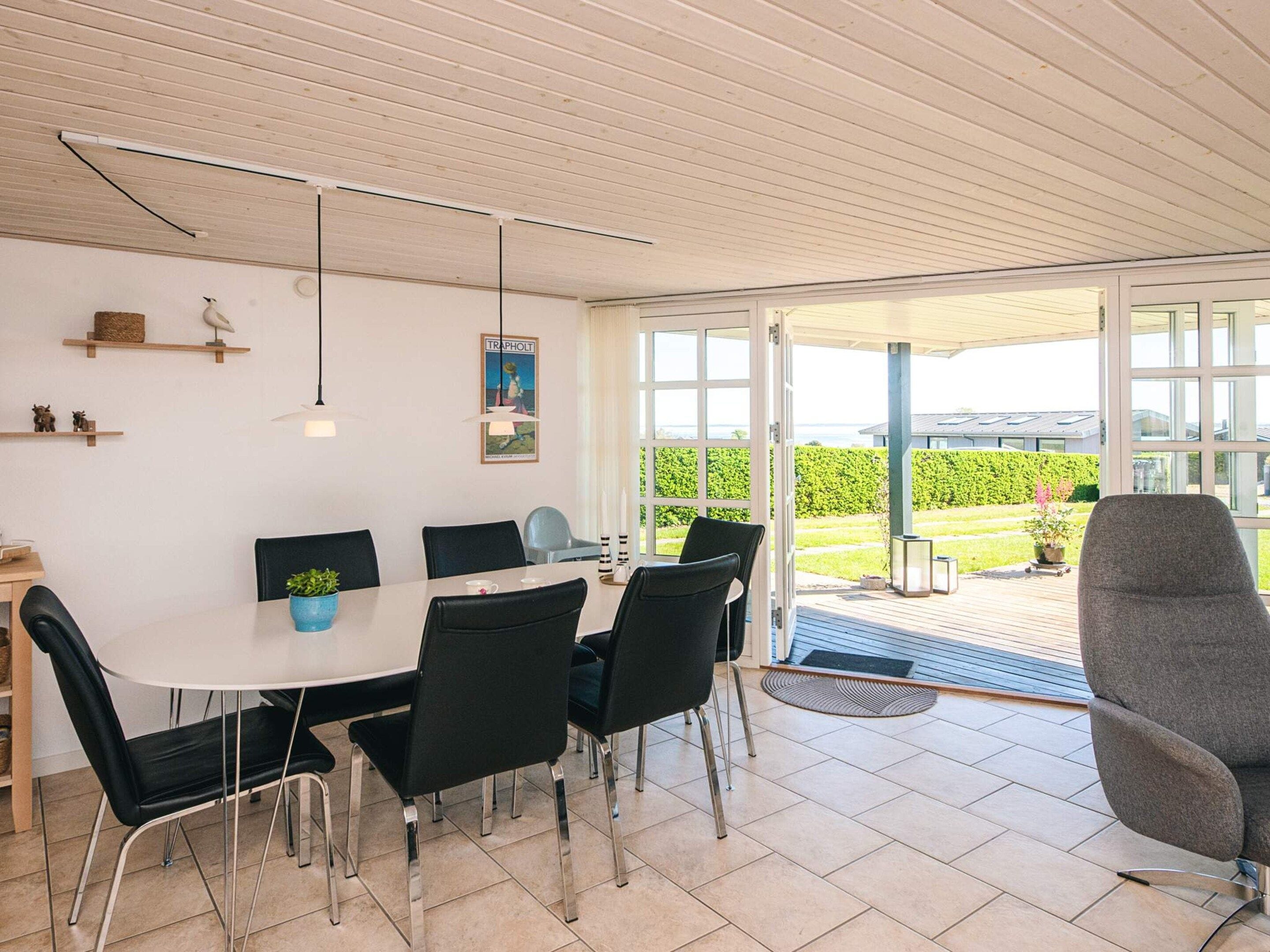Een moderne eetruimte met een witte tafel en zwarte stoelen, een potplant en uitzicht op een tuin door glazen deuren.