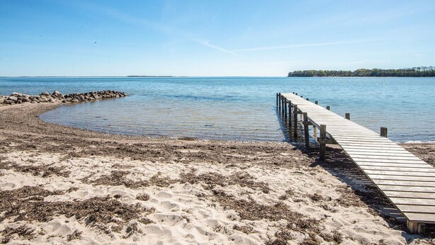 A wooden pier extending into calm waters, surrounded by sandy beach and a clear sky. - 4 Star Holiday Home in Hejls (Hejls)