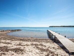 A wooden pier extending into calm waters, surrounded by sandy beach and a clear sky. - 4 Star Holiday Home in Hejls (Hejls)