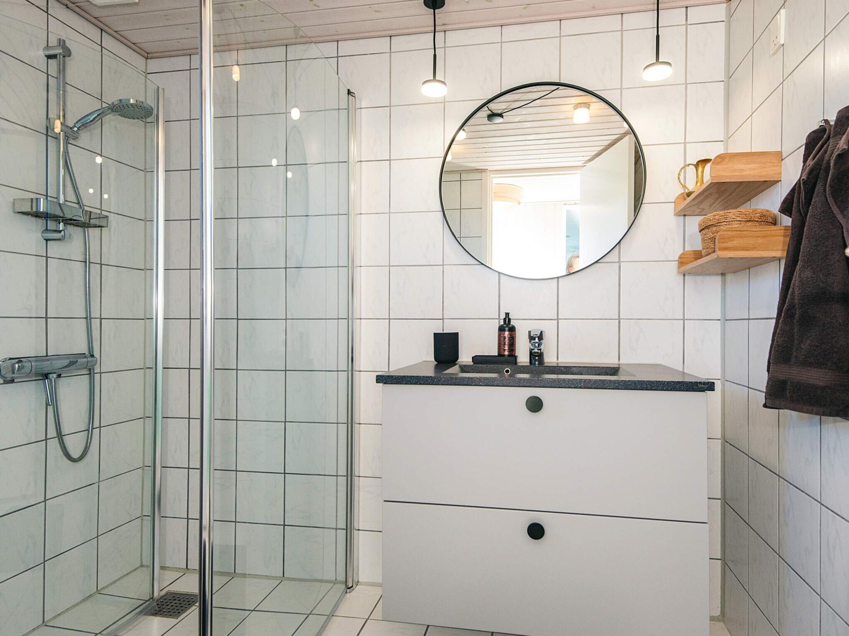 A modern bathroom with a glass-enclosed shower, a round mirror, and a vanity with a sink and storage drawers.