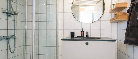 A modern bathroom with a glass-enclosed shower, a round mirror, and a vanity with a sink and storage drawers.