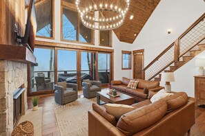 Amplia sala de estar con chimenea, ventanas grandes y una escalera de madera.