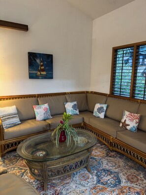 A corner seating area with a glass coffee table, patterned rug, and a painting of a sailboat.