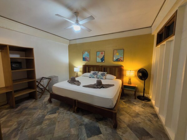 A hotel room with a bed, a ceiling fan, a bedside table with a lamp, and a floor lamp.